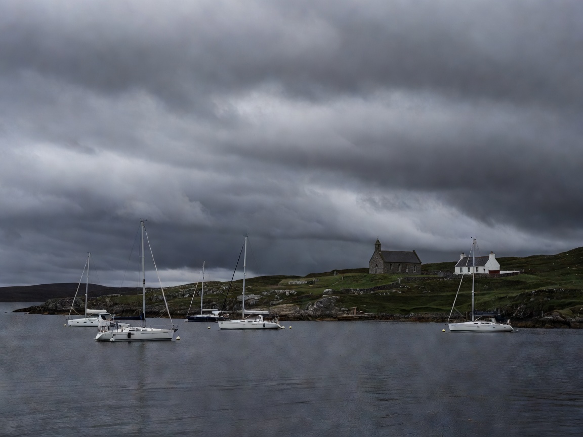 Yachts at anchor off Canna under heavy cloud with a church and farmhouse ashore