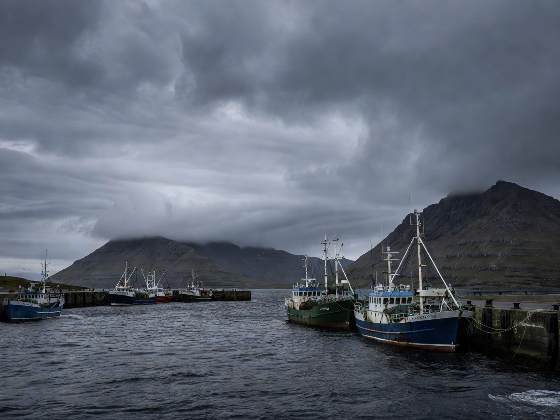 The harbour of Vágur on Suðuroy in the Faroe Islands under brooding cloud, with trawlers alongside