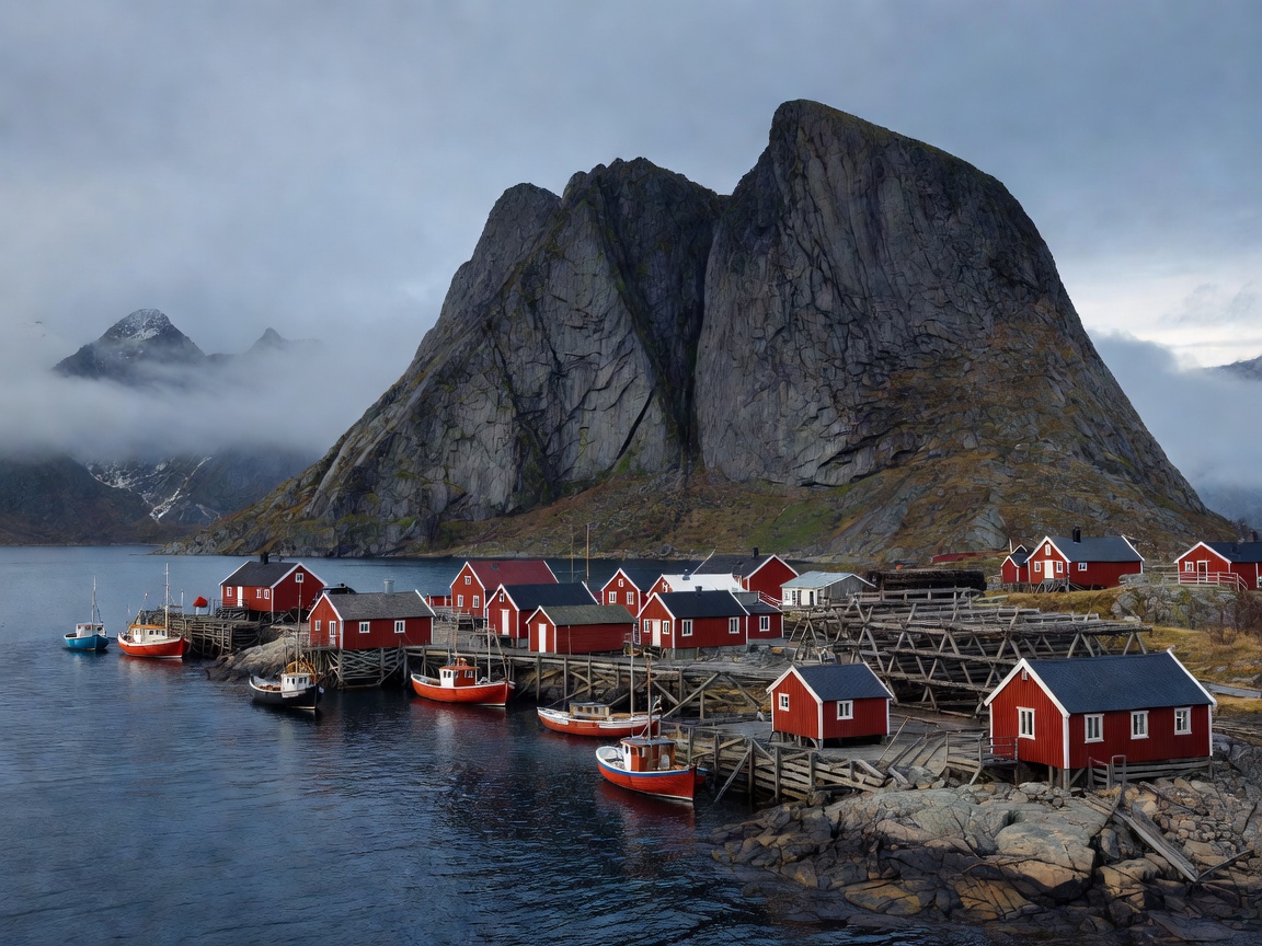 Red rorbu cabins and drying racks around the fishing harbour of Reine in Lofoten beneath dark granite peaks
